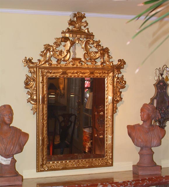 A fine giltwood Venetian mirror, the rectangular plate within a carved band of C-scrolls, flower heads, and leaf cartouche surmounted by a swagged lambrequins and feathered crest.
