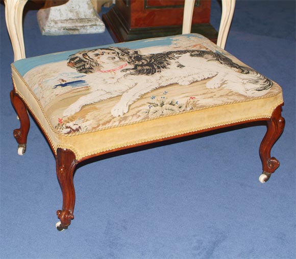 The rectangular top upholstered with a needlework panel depicting a Cavalier King Charles Spaniel beside a stream and a picket fence, below a blue sky scattered with clouds, trimmed in velvet,  raised on cabriole legs ending in scrolled feet on