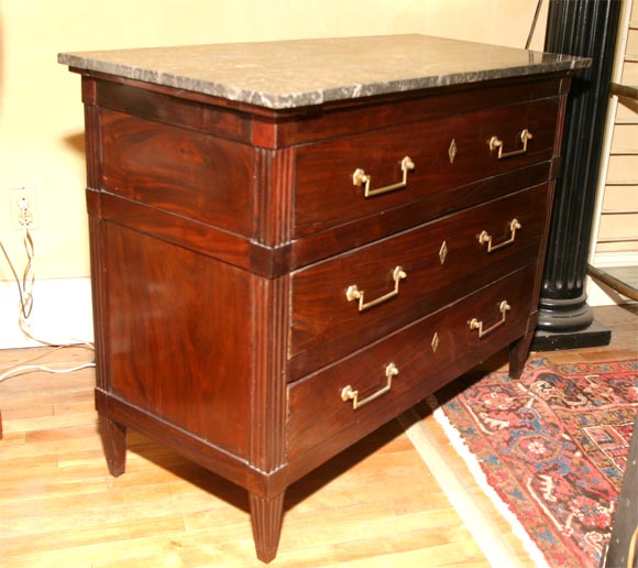 A pair of three-drawer Directoire commodes. One retains its original shaped fossil marble top, the other has a faux marble top.