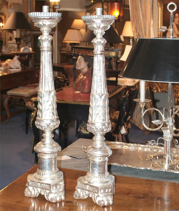 Ornately carved candlesticks with original metal drip pans, front is silvered with the opposite side painted a gray/blue color, all resting upon a tripod base