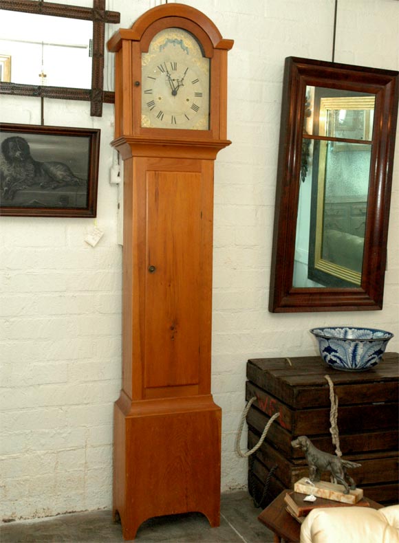This American thirty hour longcase clock has an early 19th century movement with wooden gears. The attractively hand painted arched dial shows: roman numerals for the hours, arabic numbers for the seconds, simulated winding holes and simple but