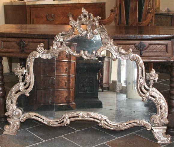 Italian rococo silver-gilt over-mantle mirror, the shaped plate surmounted by a carved, feathered crest over a rocaille and scrolling acanthus bordered mirror slip, continuing to c-scrolls, floral and berried scrolling acanthus.