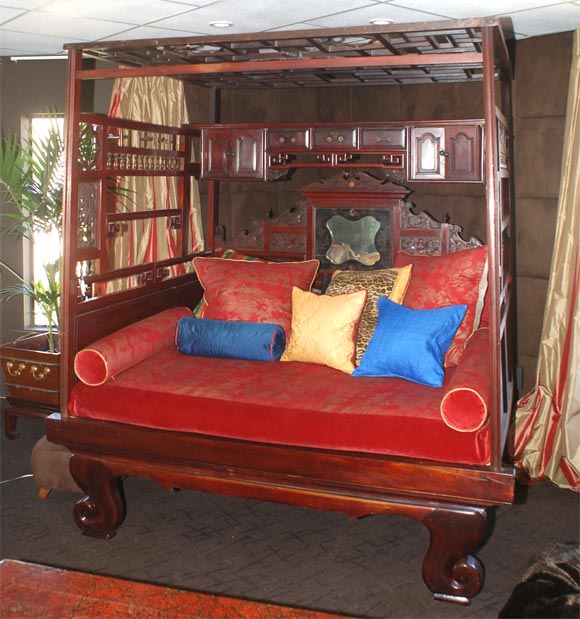 With a three-cornered canopy of latticework and carved flowers, over a head rest of dragons and flowers surrounding a painted mirror, on a scrolled leg base. Incorporating a (moveable) shelf with two compartments and three drawers .