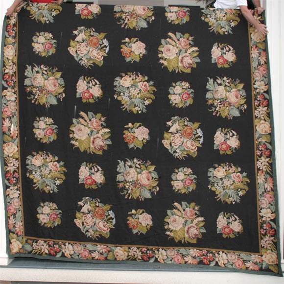 A rather large scale vintage needlepoint rug with a black ground puncuated by alternaing large and small bouquets of multicolored flowers and surrounded with a floral border.  
Roughly 13 by 16 feet. The rug is bold and impactfully but has a fine