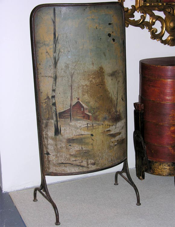 An unusual hand-painted metal firescreen with a wrought iron frame and stand; the painting is of a rural winter scene.