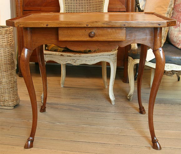 18th century walnut table with hoofed feet, scalloped apron and one drawer with leather top.