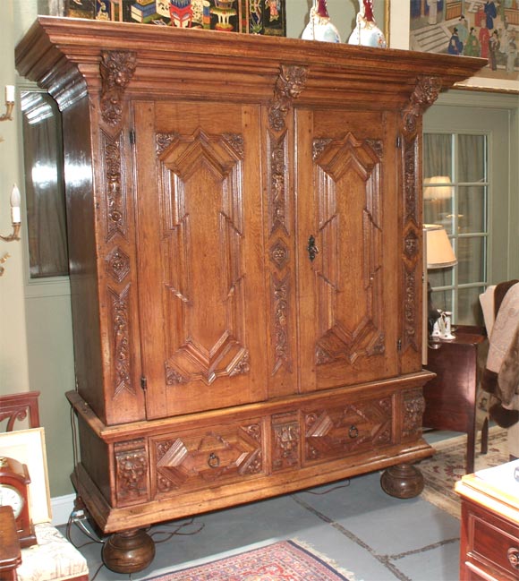 With a raised cornice atop two carved doors over two drawers resting on ball feet.