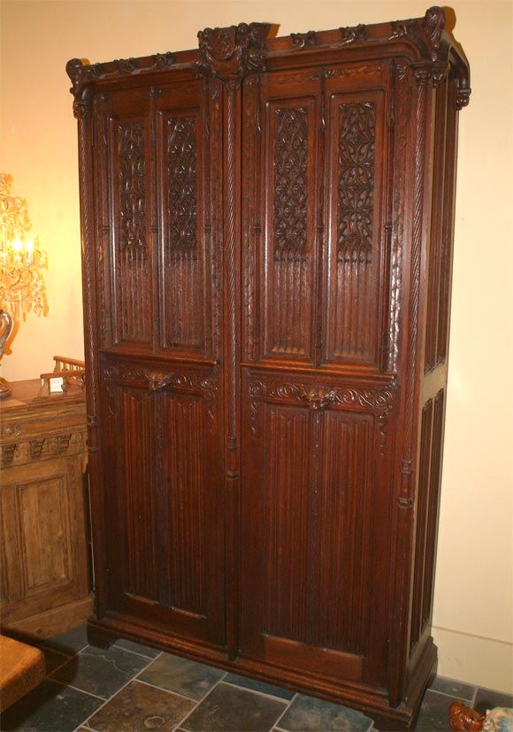 French carved oak, gothic cabinet, the scrolling foliage-carved cornice centered by an amorial crest, flanked by two angels over a case fitted with two doors, carved with inter-locking arches, flanked and separated by engaged spiral columns, raised