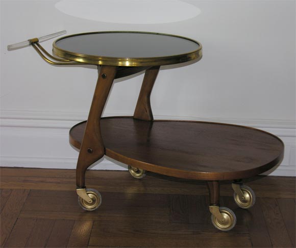 Sweet rolling cart by Russell Wright, with a Lazy Susan top in black laminate, an undershelf in walnut, brass wheels and a brass and lucite pull.<br />
<br />
Metallic label to underside.