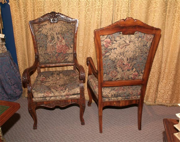 A FINE PAIR OF CARVED FRUITWOOD ARMCHAIRS EACH WITH AN ARCHED PADDED BACK WITHIN A MOLDED FRAME ON DOWNSROLLED ARMS. THE FRAME DEEPLY CARVED WITH FLOWERS, LEAVES, AND ROCAILLE. EACH TAPESTRY PANEL DEPICTING A SCENE OF FIGURES IN A FLORAL LANDSCAPE.