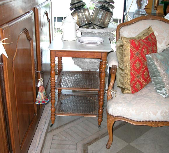 White marble top table with two cane shelves, on casters.