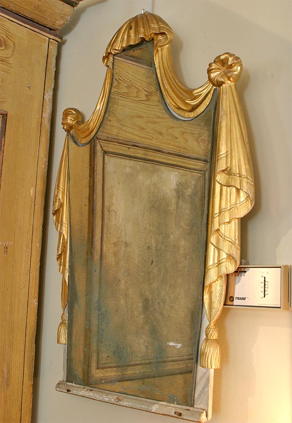 A giltwood mirror in the shape of bed canopy. The mirror is antiqued.