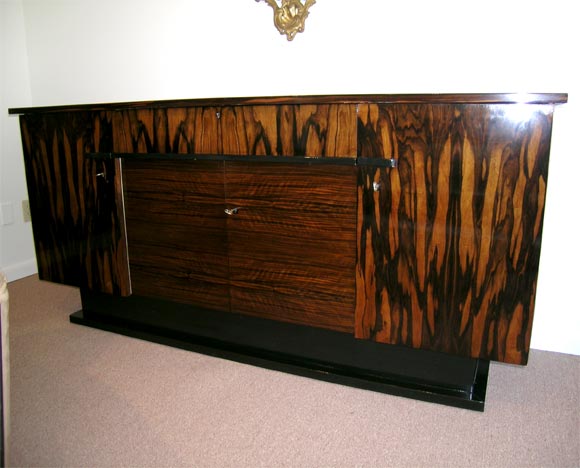 A Art Deco sideboard in Macassar Ebony on a ebonised plinth base with ebonised pulls. The sideboard features two side doors, two central doors which use a tighter grained horizontal Macassar veneer and a central top middle drawer. The sideboard has