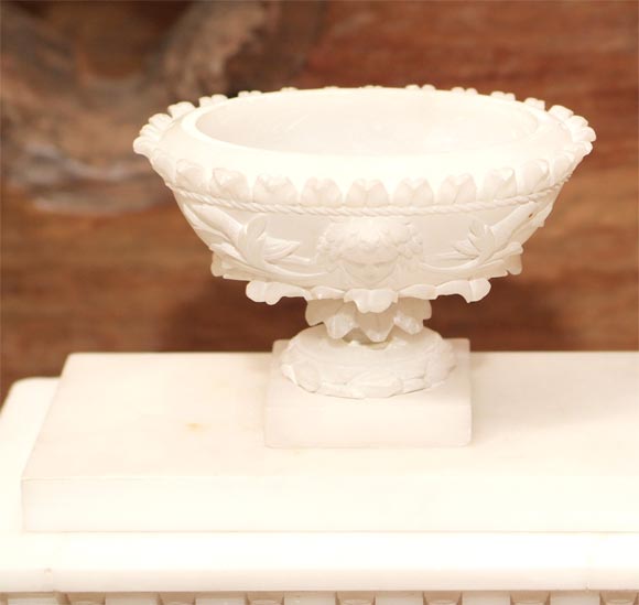 Topped with an urn finial and dentillated cornice surmounting a rectangular case applied with relief-carved florettes and a floral swag, centering a gilt-metal and enamel sunburst dial with Roman chapter numerals inscribed 