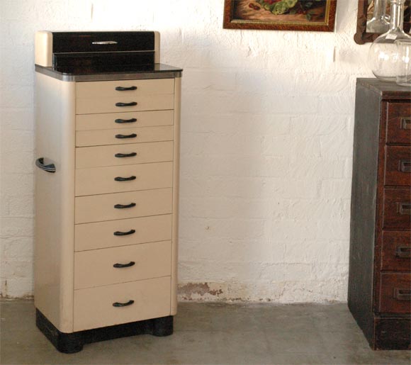 This dental cabinet, with ten drawers, is a great size for a number of uses. The cabinet is constructed in metal and wood having an oyster and black paint finish. The cabinet has a metal manufactures label affixed to the back and was made by the