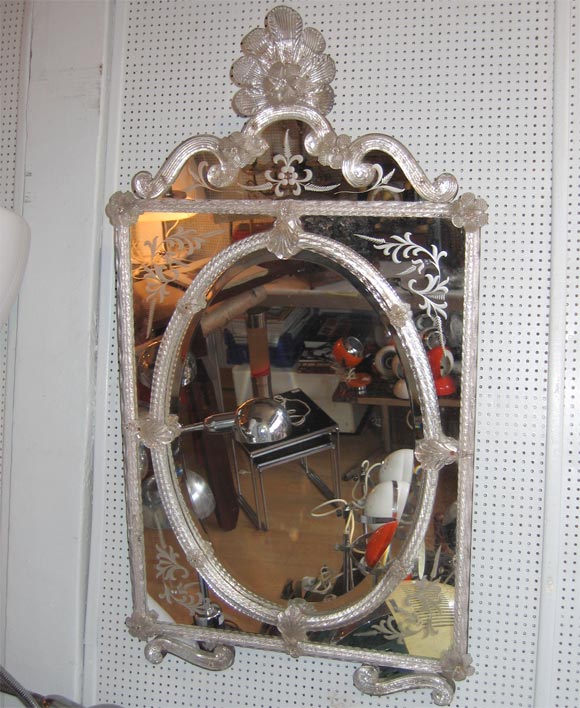 Italian mirror with an oval set in a square outer form. Engraved and applied glass decorations.