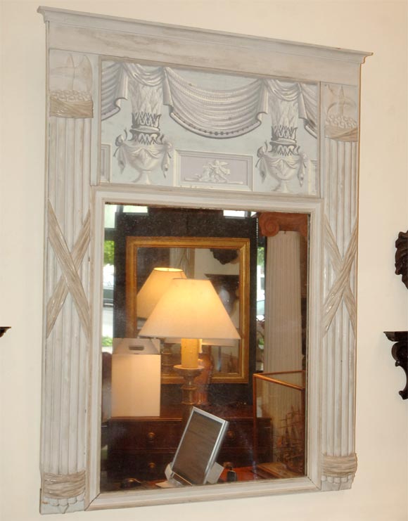 A decorative grey and white painted mirror incorporating carved wood trophies and wood blocked printed neoclassical paper panel. Italy, circa 1890.