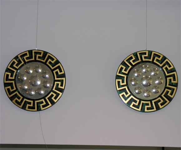 Each broad circular frame printed with a Greek key motif in black and gilt on a malachite ground, with a circular mirror cut with nine convex circles.