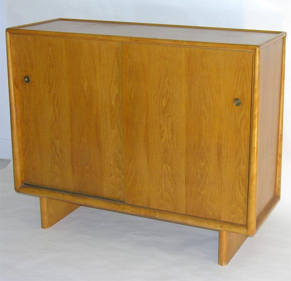 A handsome gentleman's chest framed in tapered carved dowels and two sliding doors with recessed brass pulls, concealing a variety of drawers for every purpose, model. no. 1303, by T.H. Robsjohn-Gibbings for Widdicomb. U.S.A., circa 1950.