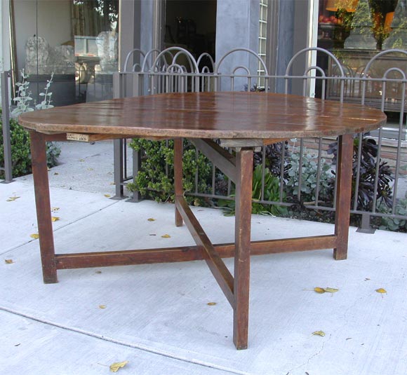 A large round folding table in pine with an X-stretcher base. This beautiful rustic table comes from a winery where it was used for tastings. The top lifts up off of the base and the base folds.