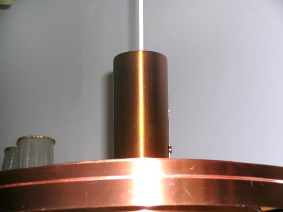 Skandinavisch-moderne Kupfer-Deckenleuchte, aufgehängt an einer verstellbaren Schnur. Die Leuchte besteht aus konzentrischen Ringen aus Kupfermetall, die das Licht gleichmäßig in den Raum reflektieren. Die Höhe ist verstellbar und das Stück kann
