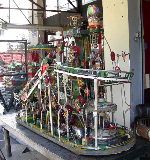 Spectaculaire et exceptionnel manège en état de marche sur le thème de la fête foraine. Composé entièrement de jouets de l'époque. Grande roue, course de motocyclettes, avions, etc.etc. Vendu avec une peinture d'un clown.