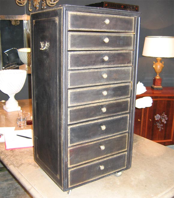 Black leather filing cabinet with gold stamping. Nine drawers with bronze pulls, locks and keys. On casters.