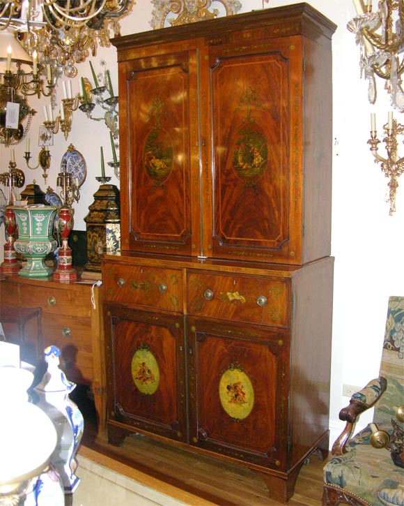A George III period two-part linen press with figured mahogany recessed panel doors in open section concealing fitted interior with adjustable shelves and lower section of greater depth having trompe l’oeil design resembling pullout desk and with