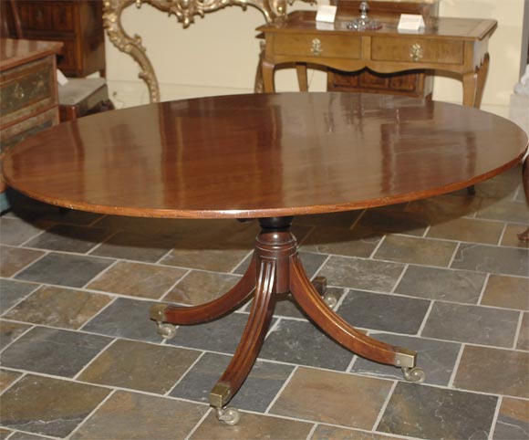 Regency mahogany tilt-top breakfast table, the oval top above an urn-turned stem, joined by four fluted sabre legs, terminating in square-cup castors.