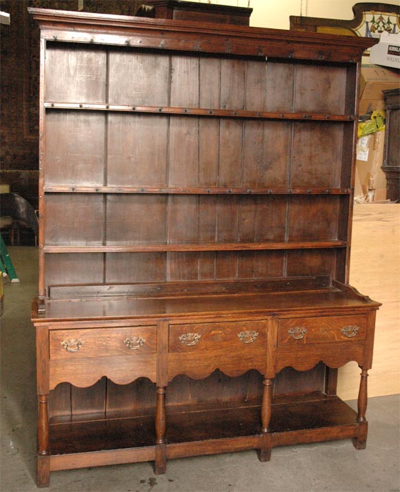 This period oak dresser has: a top section with open shelves above three drawers in the shaped frieze and with a potboard below. Height of base is 30 3/4. Dresser rests on six short block feet. Jefferson West Antiques offer a large variety of