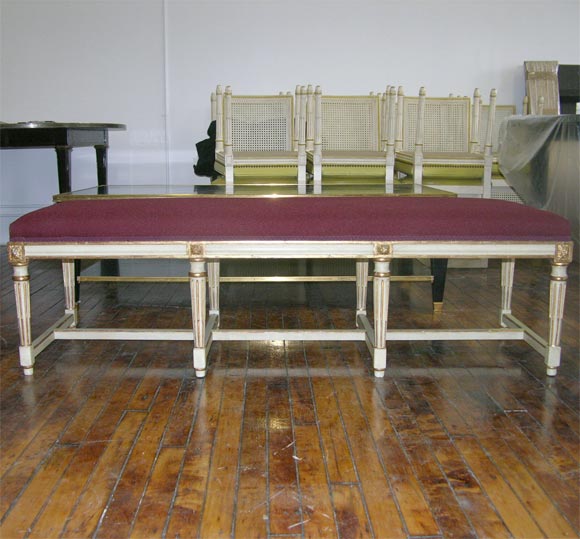 Louis XVI style gilt and painted banquette by Jansen. Raised on fluted legs joined with white and gild stretchers. Upholstered in red fabric, galon in a complementary color.  Provenance: Estate of Geraldine Stutz.