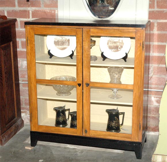 This cabinet is very pretty and useful, has two bar glazed doors and stands on a black painted base with four tapered legs. The shelf and interior is painted a pale cream. The escutcheon and other details are accented in black. 