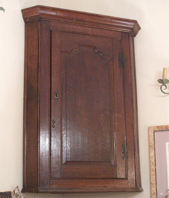 Handsome 18th century English oak hanging corner cabinet with three interior shelves; the simple carved door and frame are surmounted by a two-piece cornice. The cabinet is 30