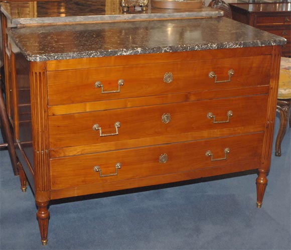 The molded edge grey marble top above three long frieze drawers flanked by stop fluted stiles raised on tapering fluted legs ending in brass caps