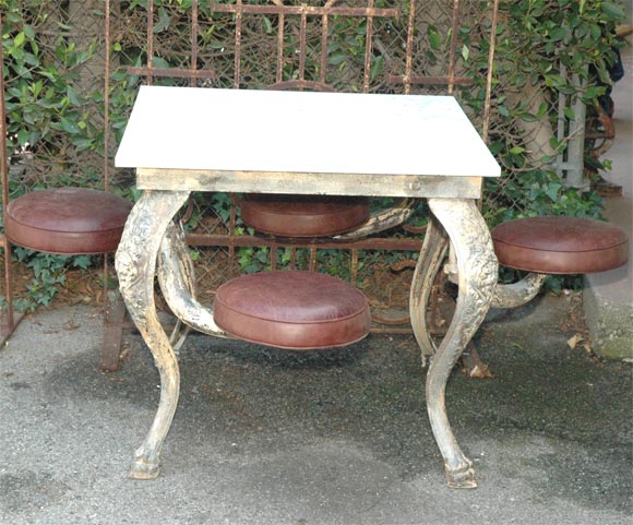 Late 19th Century American cast iron table with swivel seating. Distressed marble top. Lions faces cast in the legs with hoof feet. An original and chraming piece. Seats swing out 13