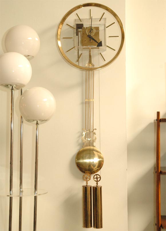 Howard Miller wall-hanging clock with a Lucite front. brass works, weights and pendulum.