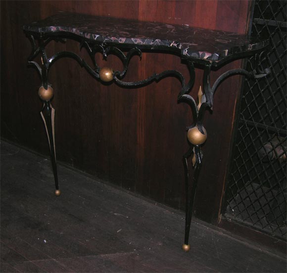 Shaped honed black marble top on Poillerat type stylized wrought iron base console with gilt ball ornamentation.