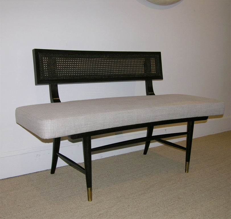 The curved back with cane panel and curved upholstered seat, supported on a tappering saber legs with brass sabots.