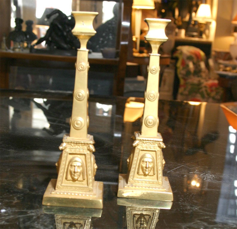 An interesting pair of gilt bronze Egyptian Revival candlesticks with a very architectural feel and dramatic facial reliefs and the lower pylon shaped base embellished with central masks.