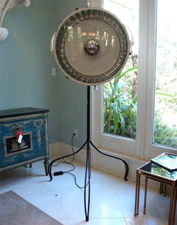 Large adjustable floor lamp manufactured by Scialytique, so marked; the reflector in white painted steel, surrounded by  mirrors at the inner edge; the lamp enclosed by a polished magnifying lens; the whole yoke-mounted to the tri-pod iron support