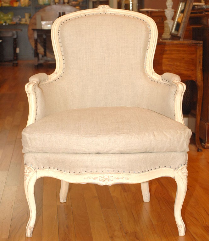 In the style of Louis XV, these chairs feature a polychrome cream painted finish and hand carved floral motif. Upholstered in French linen with flat nail head trim. Sold as pair.