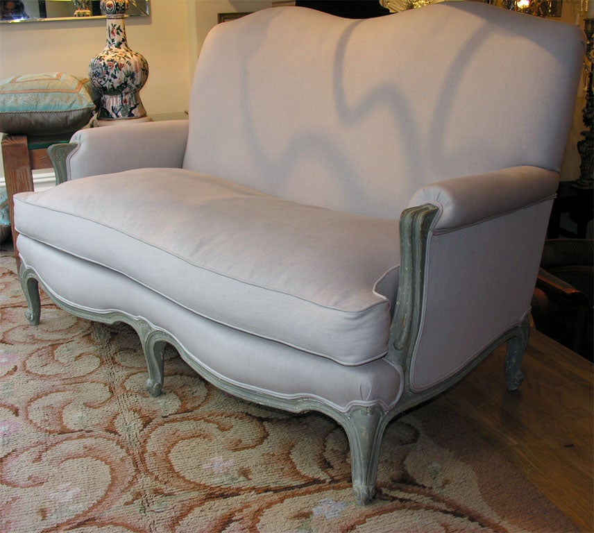 A French Louis XV style sofa with serpentine front and back having painted wooden frame with six cabriole legs and armrest upholstered with tight back and loose seat cushion. In the manner of Jansen.