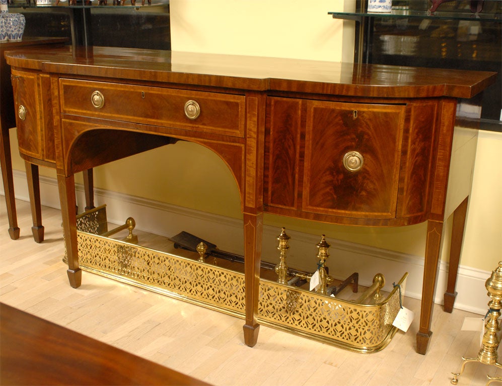 A spectacular breakfront sideboard, with bow-front side sections, influenced by the Hepplewhite school of design. Embellished with satinwood banding and inlay, and composed by a fine mahogany body. The piece is divided into three compartments, one
