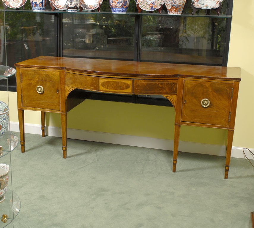 A finely patinated mahogany sideboard, with inlay and banding in sandalwood, and radiating marquetry designs in the mid-section.<br />
<br />
The body is composed of a central sliding drawer with an elegant oval inlay and flanked by two hinged