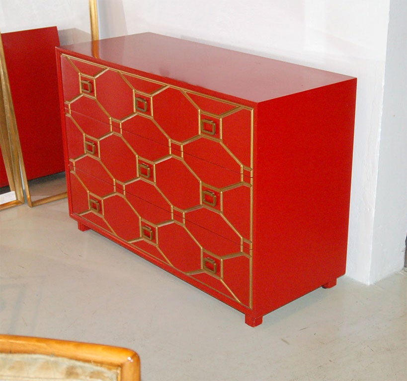 Red lacquer highlighted by dark gilding in geometrically engraved deep lines in the drawer fronts forming an overall trellis pattern. 3 drawers. Nine square pulls add form to the front panel.  Signed 