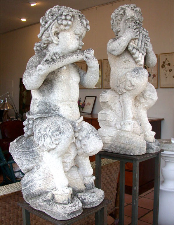Pair of carved limestone garden figures. Cherubs playing Pan Flutes. The figures have animal legs with hooves.