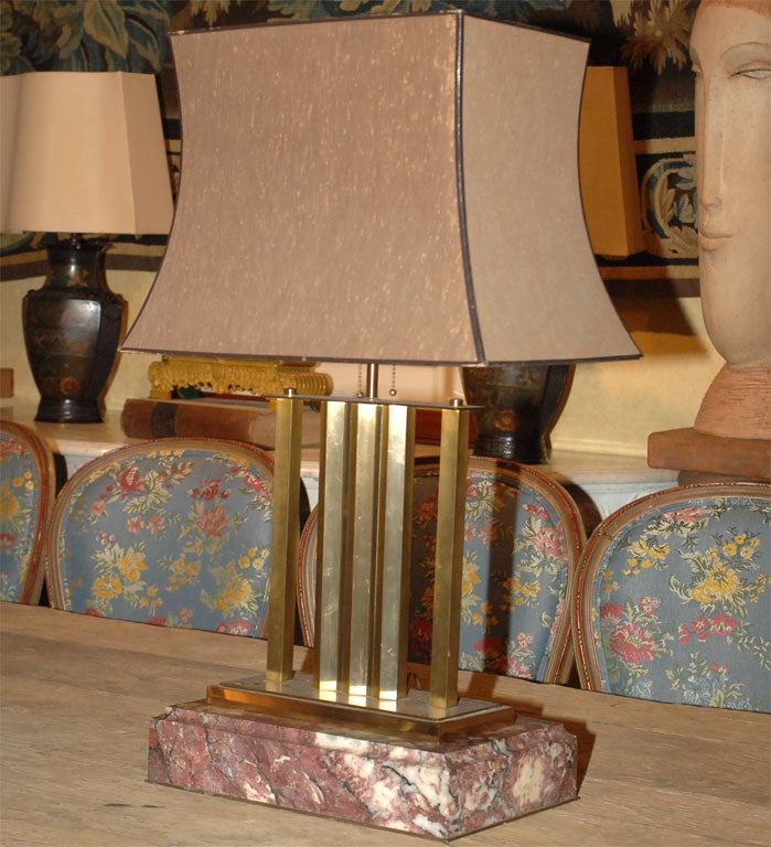 EXTREMELY STYLISH ART DECO FOUR COLUMN  BRASS LAMP RESTING ON A MARBLE PLINTH. THE LAMP IS NOT ATTACHED TO THE PLINTH WHICH CAN BE USED SEPARATELY.A BANDED SHAPED OCHRE COTTON SHADE COMPLETES.