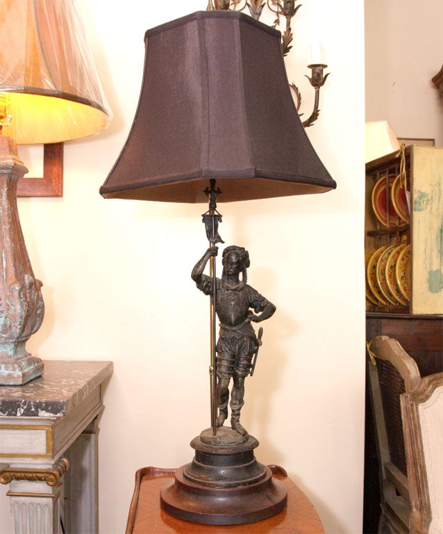 Lamp with black linen shade, featuring an iron figure of a soldier holding a staff, mounted on a wooden base.  The height of the lamp is 33