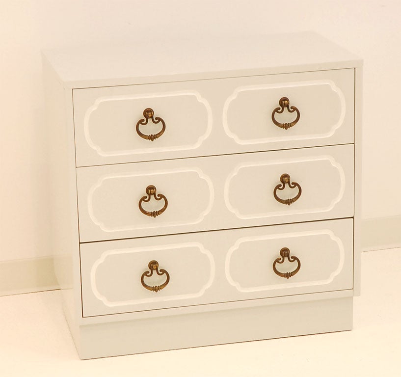 A pair of chests, with three drawers each, reminiscent of the well-known Dorothy Draper style.  The unusual bronze pulls are a striking contrast to the pale gray finish with white trim.