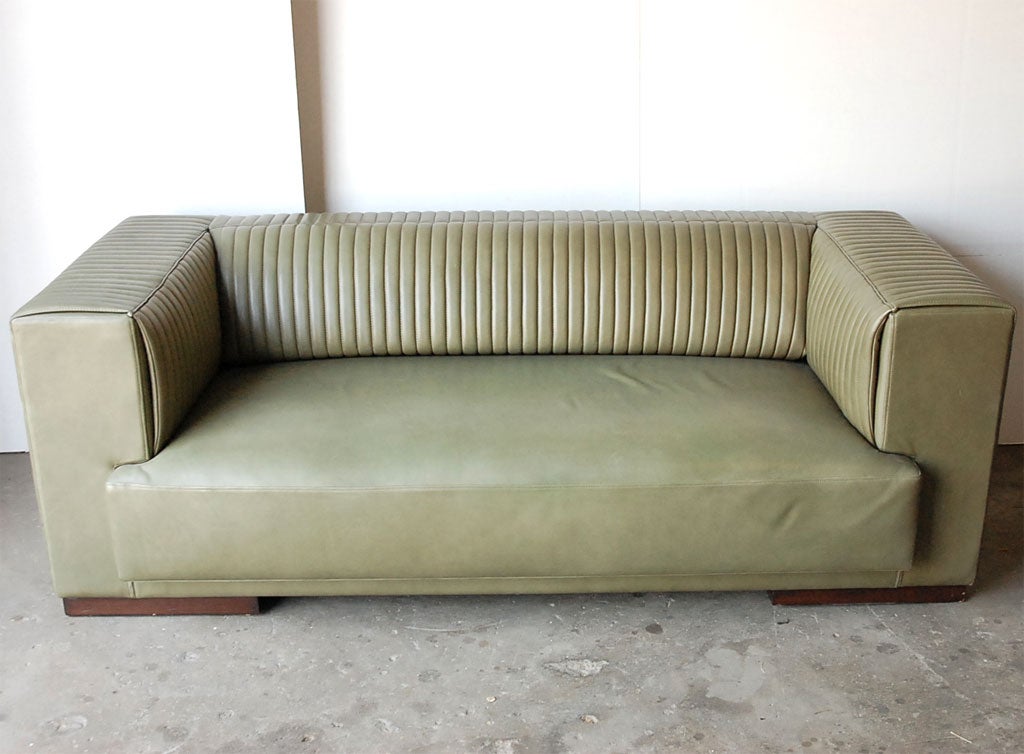 Modernist reinterpretation of a classic Chesterfield sofa, meticulously detailed with channel quilting on arms and back.  Tight seat and back. Bold proportions. Fine olive toned leather upholstery with dark mahogany feet.  This is a floor sample. 